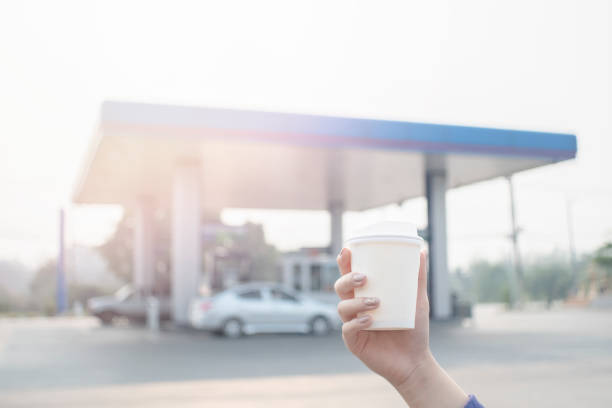 Paper coffee cup in hand the background is gas station stock photo