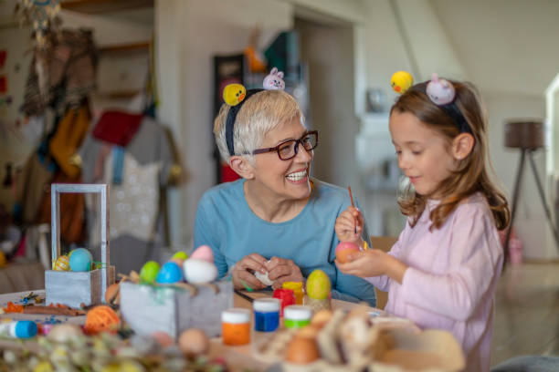 concept de pâques. belle petite fille et grand-mère heureux avec les cheveux gris préparent des oeufs de poulet pour des vacances - craft eggs easter animal egg photos et images de collection