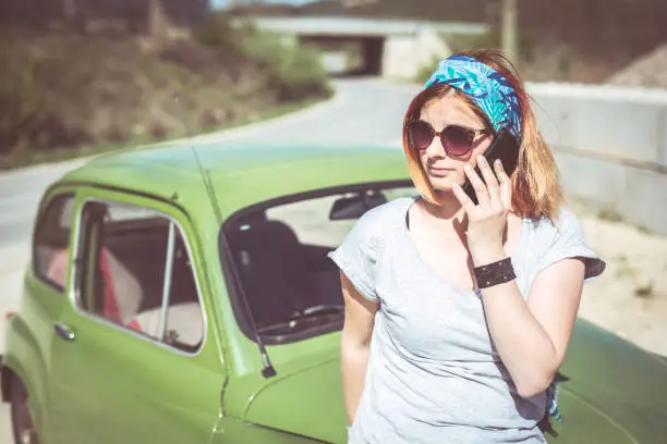 A ginger girl talking on her phone next to her restorated green supermini car
