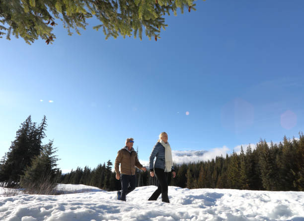 caminhada madura dos pares através da neve profunda no prado - apres ski couple love winter - fotografias e filmes do acervo