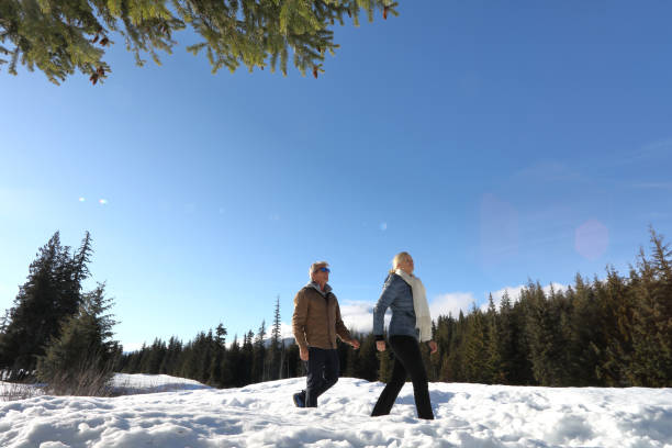 caminhada madura dos pares através da neve profunda no prado - apres ski couple love winter - fotografias e filmes do acervo