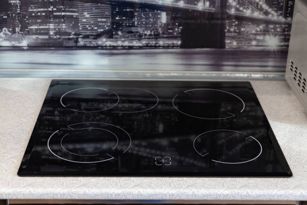 istock Four-burner black hob integrated into a white table with a black glass wall with a pattern in the kitchen at home 1140292059