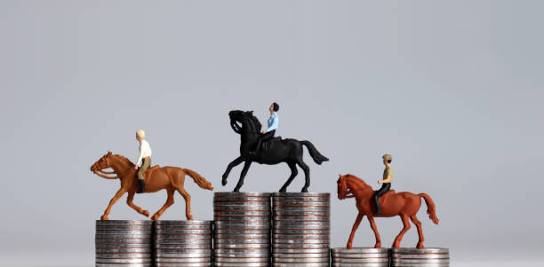 Three miniature men riding horses on piles of coin piles. Three pile of coins in the shape of a podium. stock photo