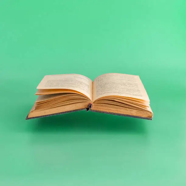 Levitating open old book on green background.  Minimal concept. Copy space