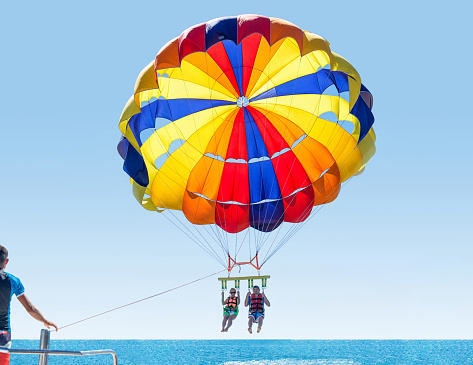 Feliz pareja sonriente parasailing en Tropical Beach en verano. Recién casados bajo paracaídas colgando medio aire. Divirtiendo. Paraíso tropical. Emociones humanas positivas. photo