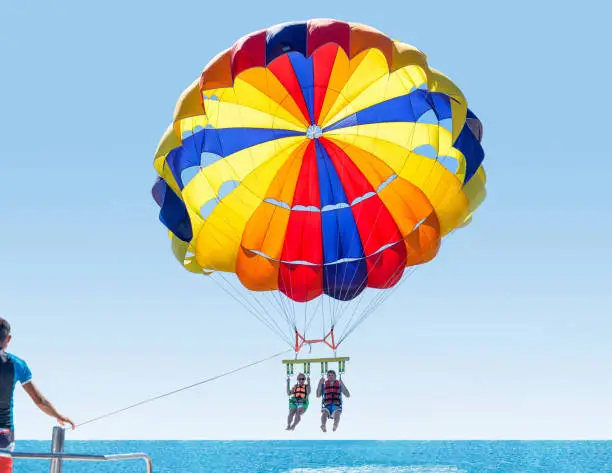 Happy smiling couple Parasailing on Tropical Beach in summer. Newlyweds under parachute hanging mid air. Having fun. Tropical Paradise. Positive human emotions.