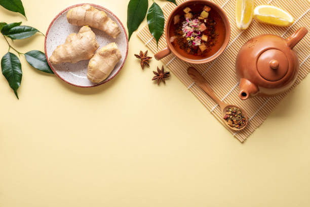 istock Flat lay composition with teacup, teapot on bamboo mat, spoon of dried tea, ginger root in plate, branches with green leaves, lemon on yellow background, top border or frame, view from above. 1140312363