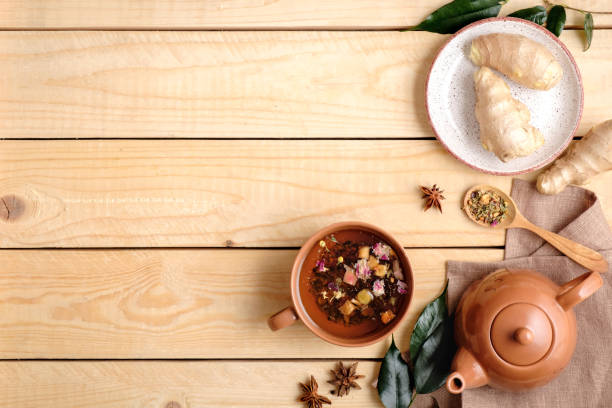 istock Tea ceremony setting with tea cup, tea pot, spoon of dried tea, anise star, ginger root on play, green leaves on wooden background. Flat lay composition. Top view 1140312364