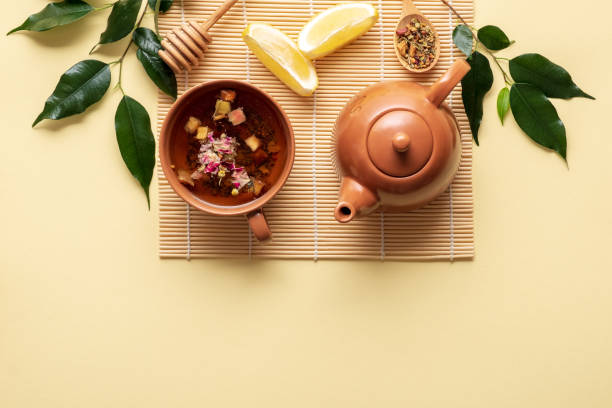 ティーカップ、ティーポット、レモン、乾燥したお茶のスプーンと緑の枝と黄色の背景に竹マット上の葉とお茶のセット。上面図、フラットレイ組成物 - tea cup tea cup herbal medicine ストックフォトと画像