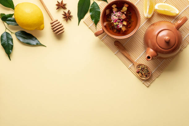 istock Tea setting with teacup, teapot, anise star, lemon, honey dipper, branches with leaves on bamboo mat on yellow background, top border, flat lay composition, view from above. Herbal tea concept 1140312370