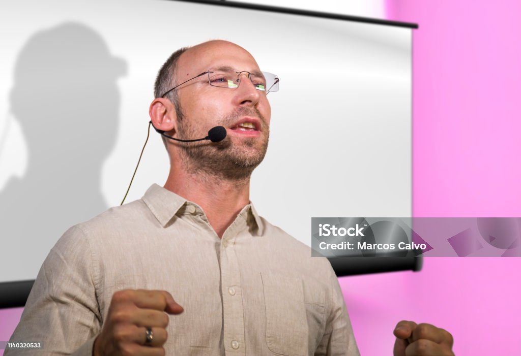 young successful and confident businessman with headset speaking at corporate business coaching and training auditorium conference room talking giving motivation training from speaker stage 30-39 Years Stock Photo
