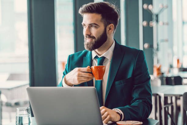Smiling Caucasian elegant businessman drinking coffee in cafe, using laptop and looking trough window. Push yourself, because no one is going to do it for you.