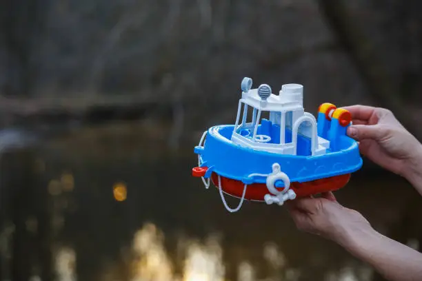 Photo of A girl holds in her hands a small toy steamer above a forest stream