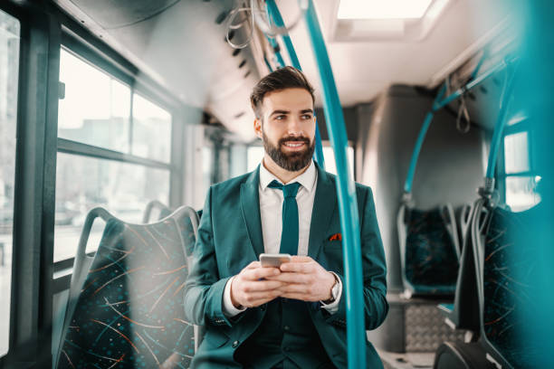 istock Smiling ambitious bearded businessman in turquoise suit sitting in public bus and using smart phone. If you want to fly, give up everything that weights you down. 1140328332