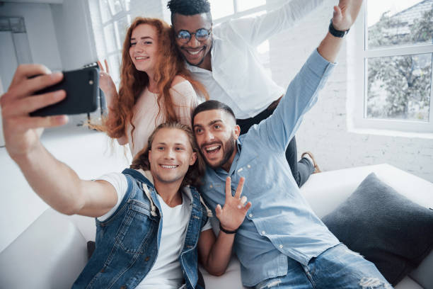 istock Show me your hands. Cheerful young friends taking selfies on sofa and white interior 1140328663