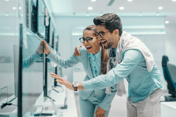 alegre pareja multicultural atractiva vestidos elegante encontrado nueva smart tv para su casa. tienda de tecnología interior. - tienda de electrónica fotografías e imágenes de stock