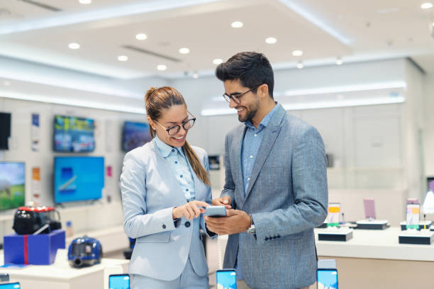 istock Smiling multicultural couple in formal wear trying out new smart phone while standing in tech store. 1140330212
