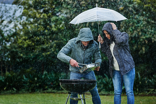Shot of a young couple having a barbecue outside in the rain