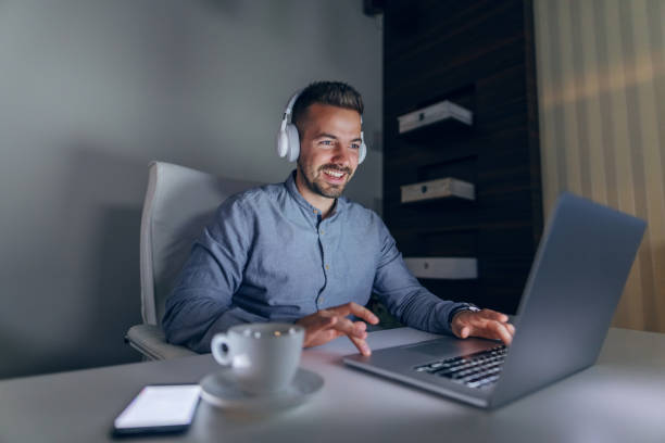 istock Young Caucasian smiling handsome bearded freelancer with headphones on ears using laptop for important project. 1140331535