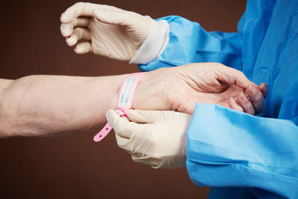 le mani guantate attaccano il braccialetto d'identità al paziente ospedaliero - braccialetto di identificazione foto e immagini stock