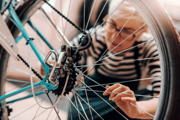 bella lavoratrice caucasica con capelli biondi corti e occhiali accovacciati e riparatrici di bicicletta. interni officina bici. - bicycle pedal foto e immagini stock