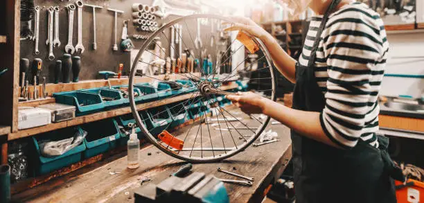 Photo of Cute Caucasian female worker holding and repairing bicycle wheel while standing in bicycle workshop.