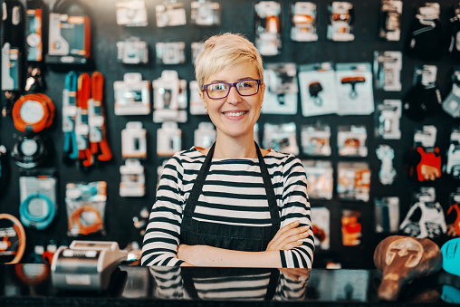 Retrato de hermosa trabajadora caucásica sonriente con pelo rubio corto de pie en la tienda de bicicletas con los brazos cruzados. photo