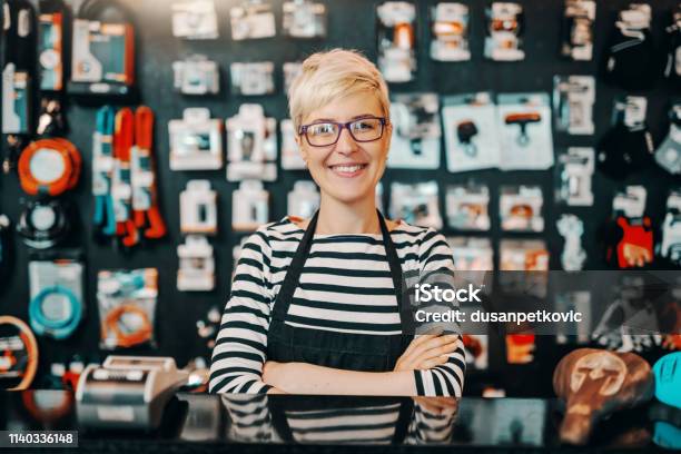 Portrait Of Beautiful Smiling Caucasian Female Worker With Short Blonde Hair Standing In Bicycle Shop With Arms Crossed Stock Photo - Download Image Now