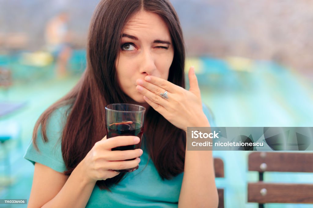 Woman Reacting after Having a Fizzy Soda Drink Funny female customer in a restaurant having a carbonated beverage Hiccup Stock Photo