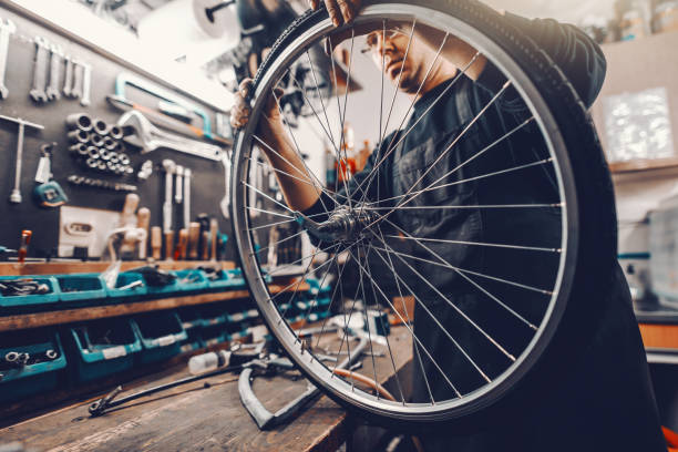 ワークショップに立っている間、自転車のホイールにタイヤを置く白人専用の男。 - bicycle shop ストックフォトと画像