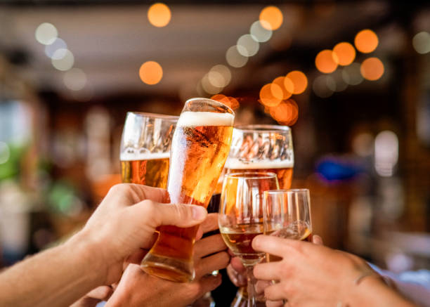 Hands of friends raising celebratory toast at bar Hands of man and woman holding drinks at restaurant. Male and female friends are raising celebratory toast. They are enjoying during party. cheers beer stock pictures, royalty-free photos & images