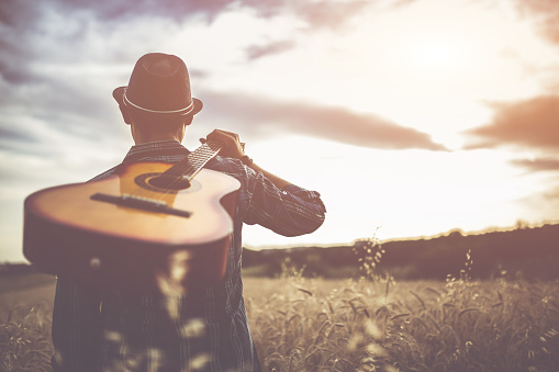 Young man walking through the wheat field with guitar on back.