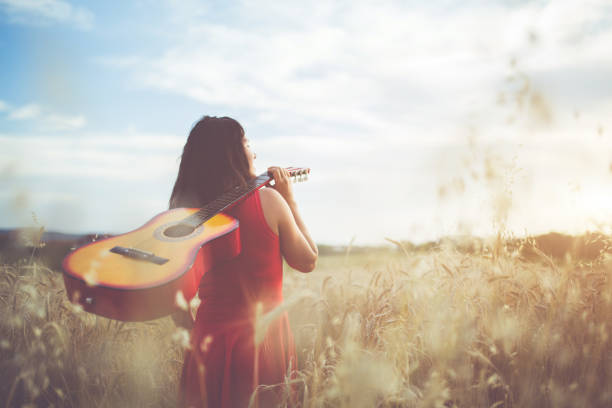 istock Woman walking through the wheat field with guitar on back. 1140341137