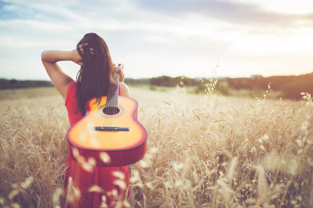 istock Woman walking through the wheat field with guitar on back. 1140341160