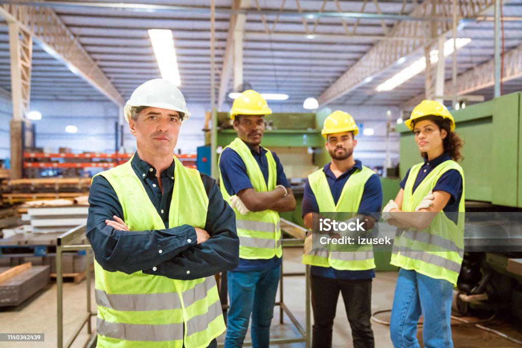 Expertise wearing reflective clothing and hardhats Portrait of confident expertise wearing reflective clothing and hardhats. Production workers are standing in factory. Colleagues are working in manufacturing company. Hardhat Stock Photo