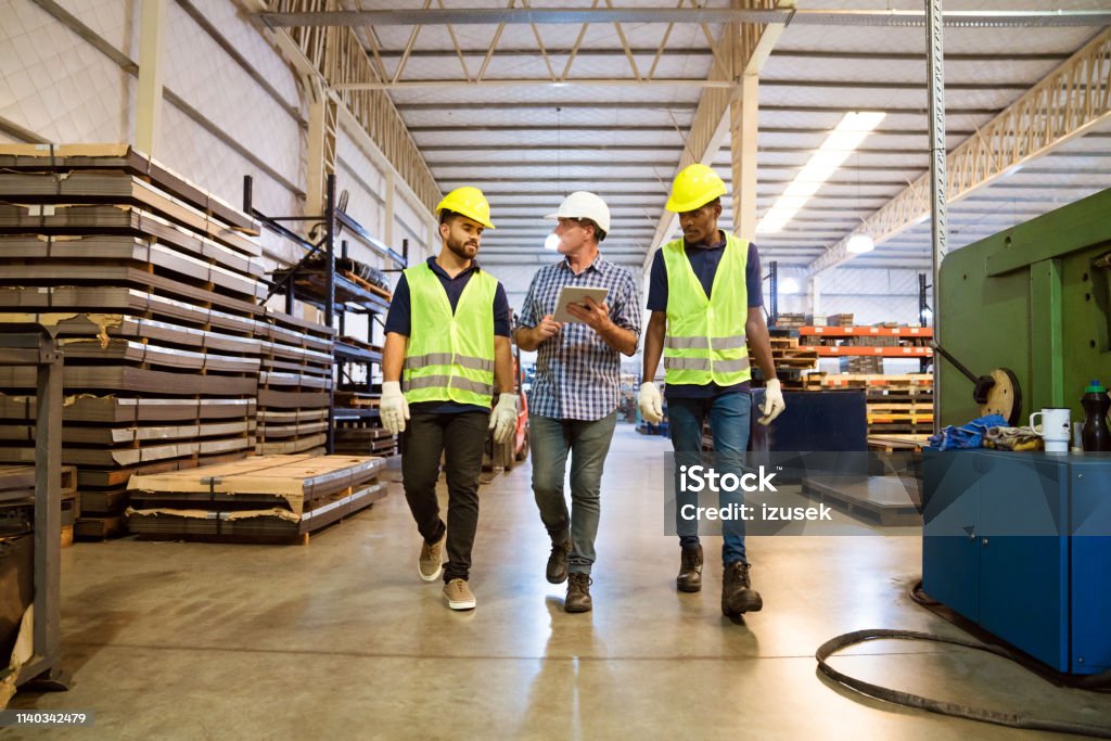 Foreman discussing with trainees in factory Foreman discussing over digital tablet with trainees. Workers are planning together in manufacturing company. They are walking in factory. Walking Stock Photo