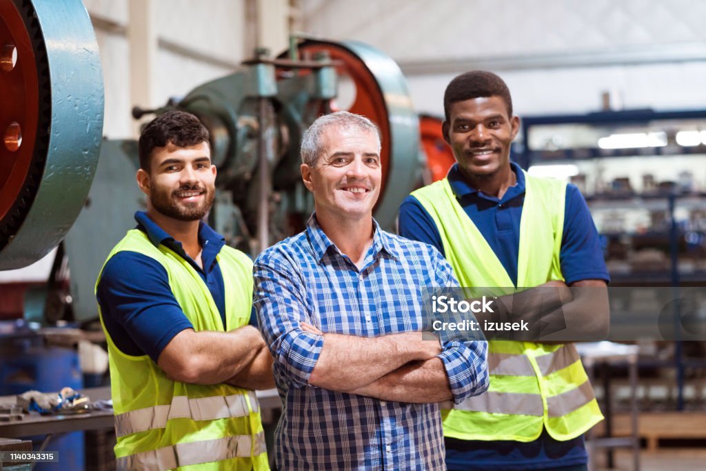 Smiling engineers with arms crossed in factory Smiling male engineers with arms crossed in manufacturing industry. Expertise are standing in company. They are with confident look on their faces. Colleague Stock Photo