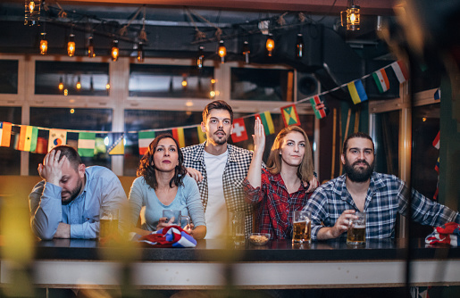 Group of young people, in a pub all together, watching a sports game.