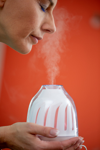 Adult Woman Holding and Inhaling Steam from Humidifier.