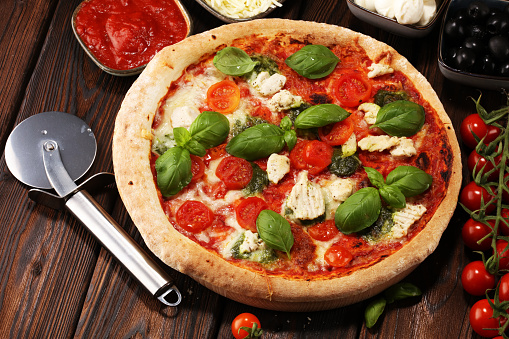 Pizza with tomatoes, mozzarella cheese, black olives and basil. Delicious italian pizza on wooden pizza board. Italian pizza