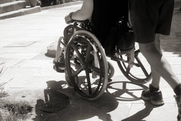 Wheelchair using young man and his girlfriend walking together through a city park on a sunny afternoon