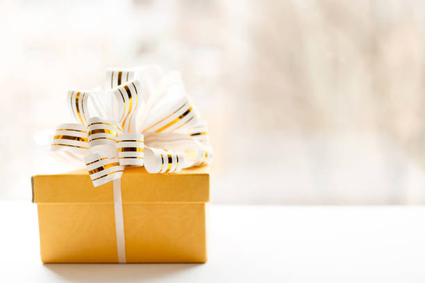 istock yellow Gift box wrapped in white and gold striped ribbon on light background. Empty note tied over. copy space . place for text 1140356640