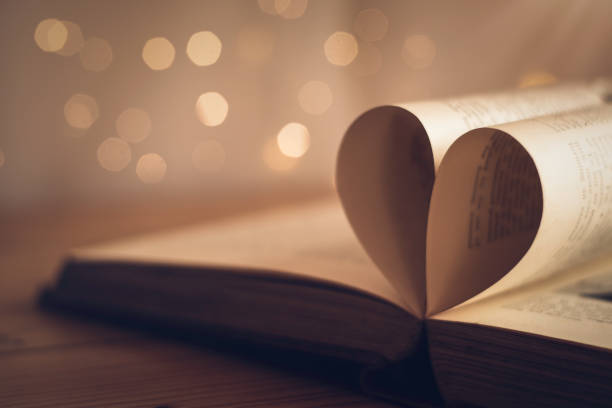 Book pages folded into a heart shape with blurred light bokeh background