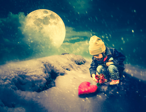 Asian girl in warm clothes holding beautiful roses with red heart on ground. Snow falling with super moon on night sky above snowy in winter. valentine's day. The moon taken with my camera.