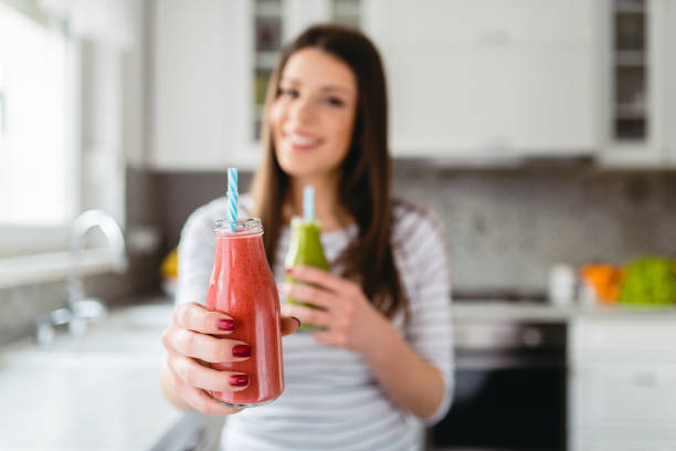 Close up of female hand holding and offering red smoothie in jar. She chose green one. stock photo
