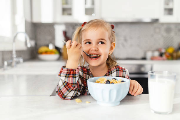 キッチンでシリアル、ミルク、ブルーベリーと朝食を持つ美しい小さな女の子 - child education human hand happiness ストックフォトと画像