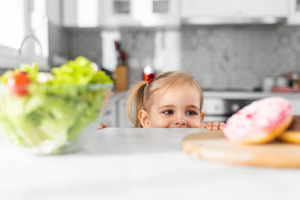 Female child chooses between donuts and vegetable salad. stock photo