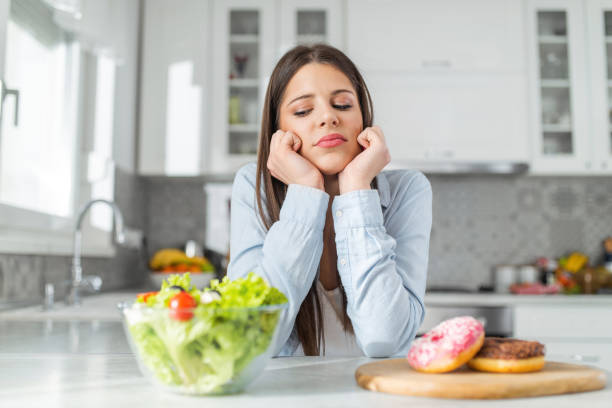 девочка-подросток выбирает между пончиками и овощным салатом - unhealthy eating стоковые фото и изображения