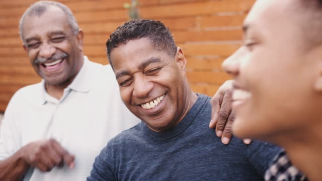 Three generations of black family men laughing together outdoors, close up