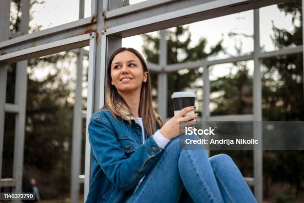 Young Woman Sitting Outside Drinking Coffee And Listening To Music Stock Photo - Download Image Now